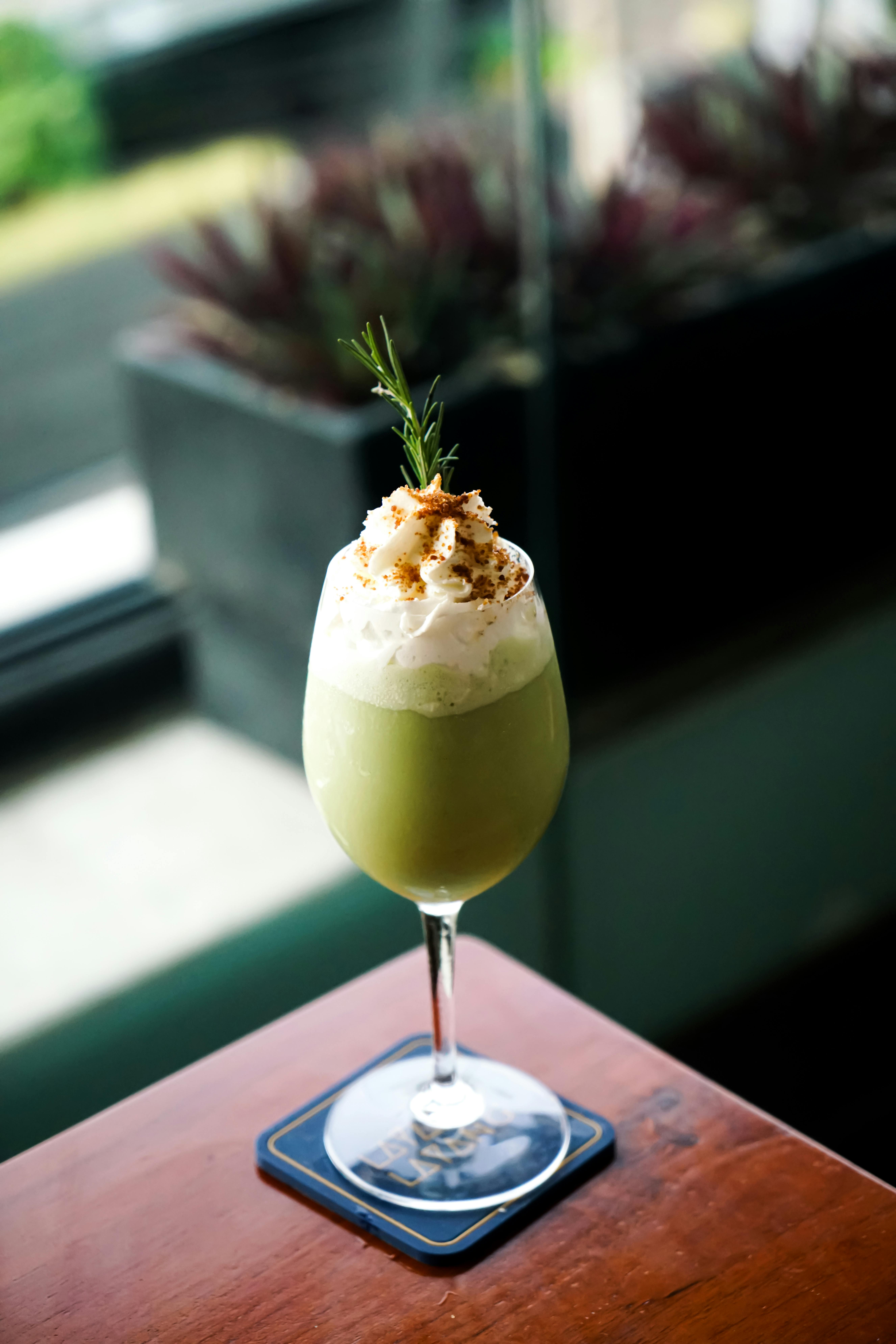Delicious green matcha latte topped with cream and rosemary in a glass, perfect for a relaxing moment.
