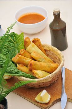 Savory spring rolls served in a basket with sauce and lemon, perfect for appetizers.