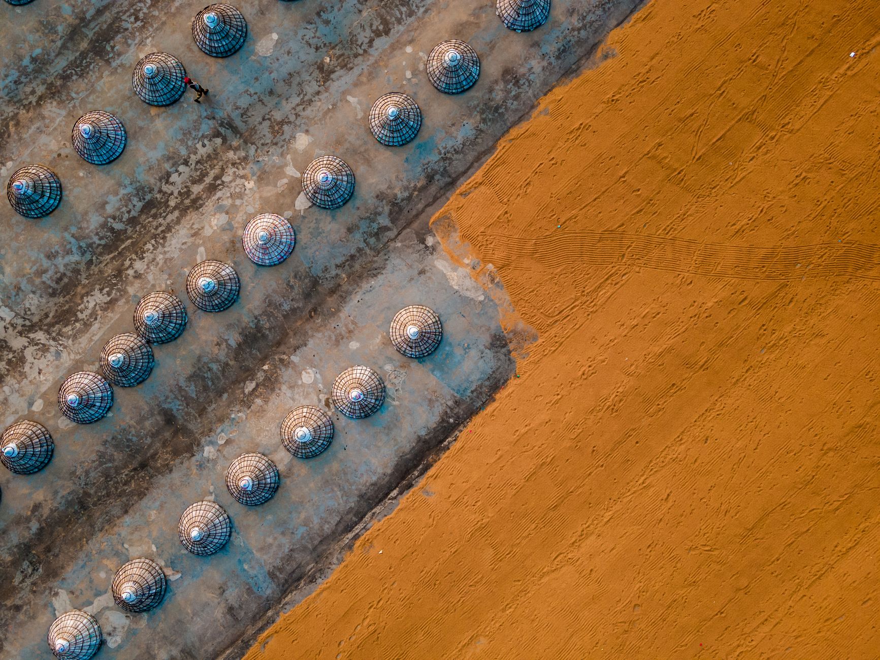 Foto de cima de estruturas com cúpulas alinhadas em uma superfície arenosa, criando padrões geométricos.