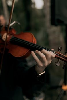 Close-up of a violinist playing outdoors, capturing the elegance of music with a dark and moody tone.