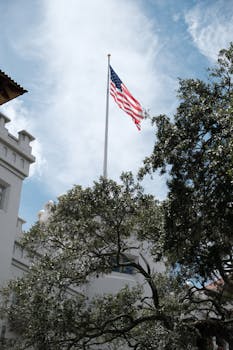 A US flag waves majestically above a historic building surrounded by trees.