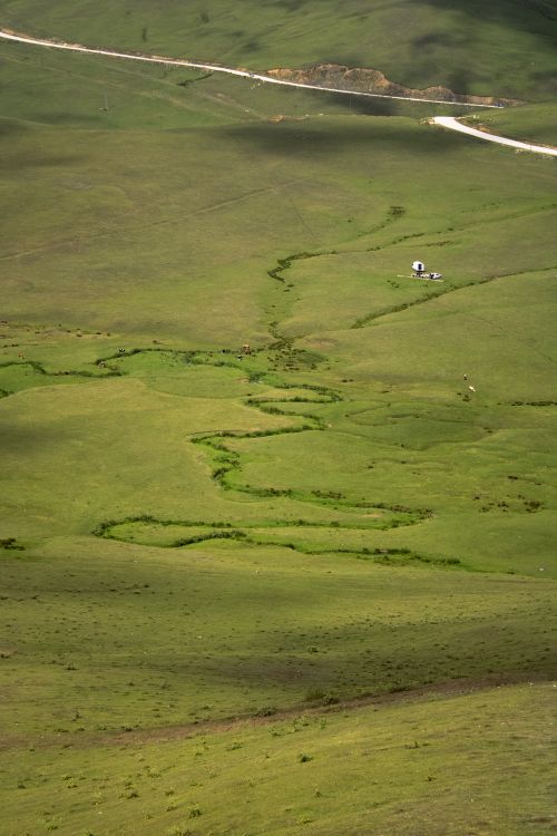 Free Aerial landscape of green hills with a small structure and winding streams, bathed in sunlight. Stock Photo