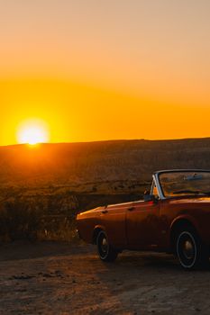 A classic red convertible car parked under a vibrant sunset in Cappadocia, Türkiye, offering a nostalgic travel vibe.