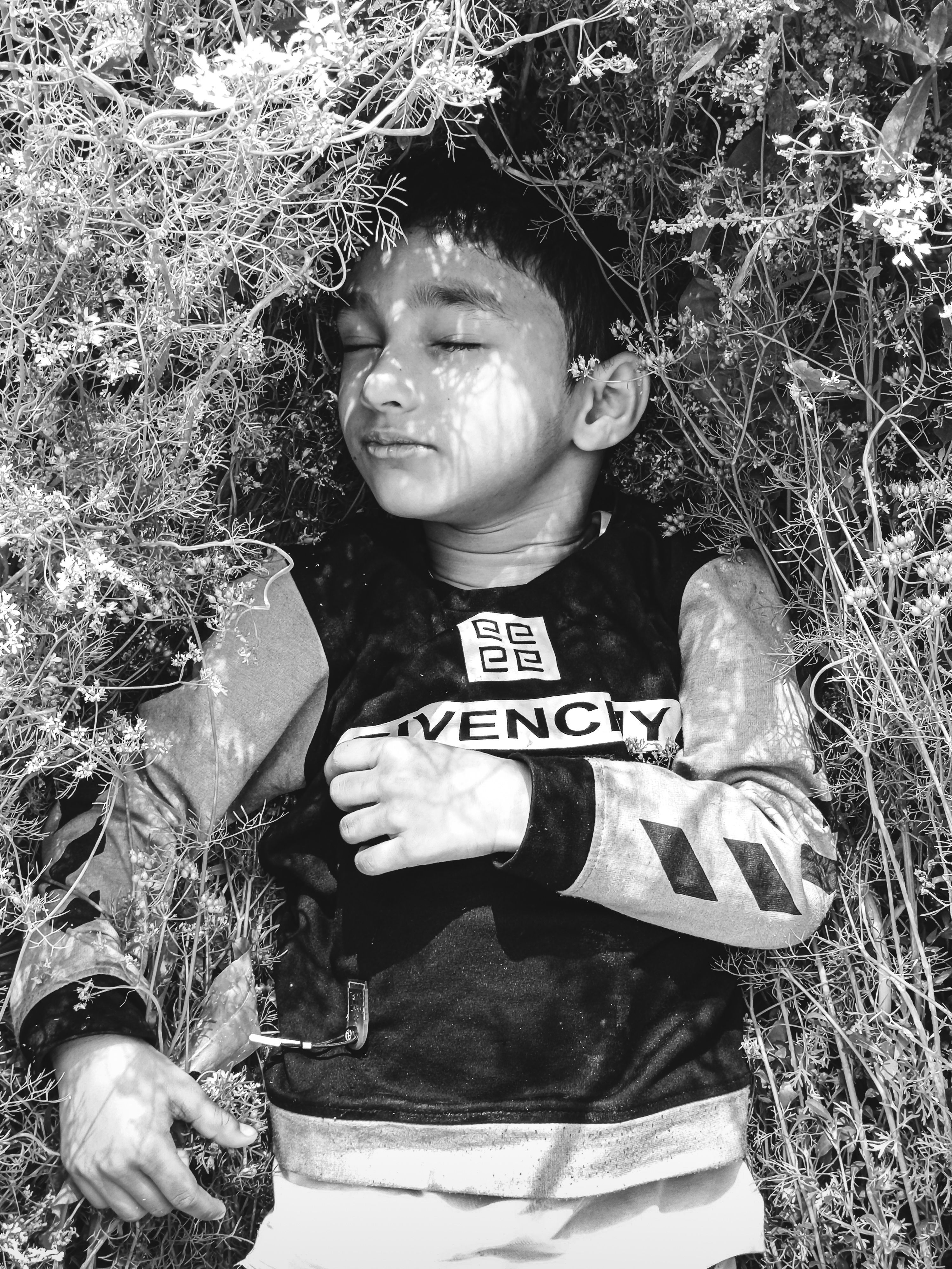 A serene black and white image of a child peacefully sleeping outdoors in nature.