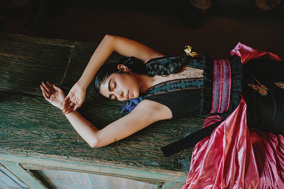 Woman in vibrant traditional attire resting dramatically on a wooden surface.