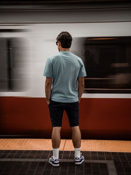 A person stands on a subway platform in Boston as a train speeds by, capturing urban life.