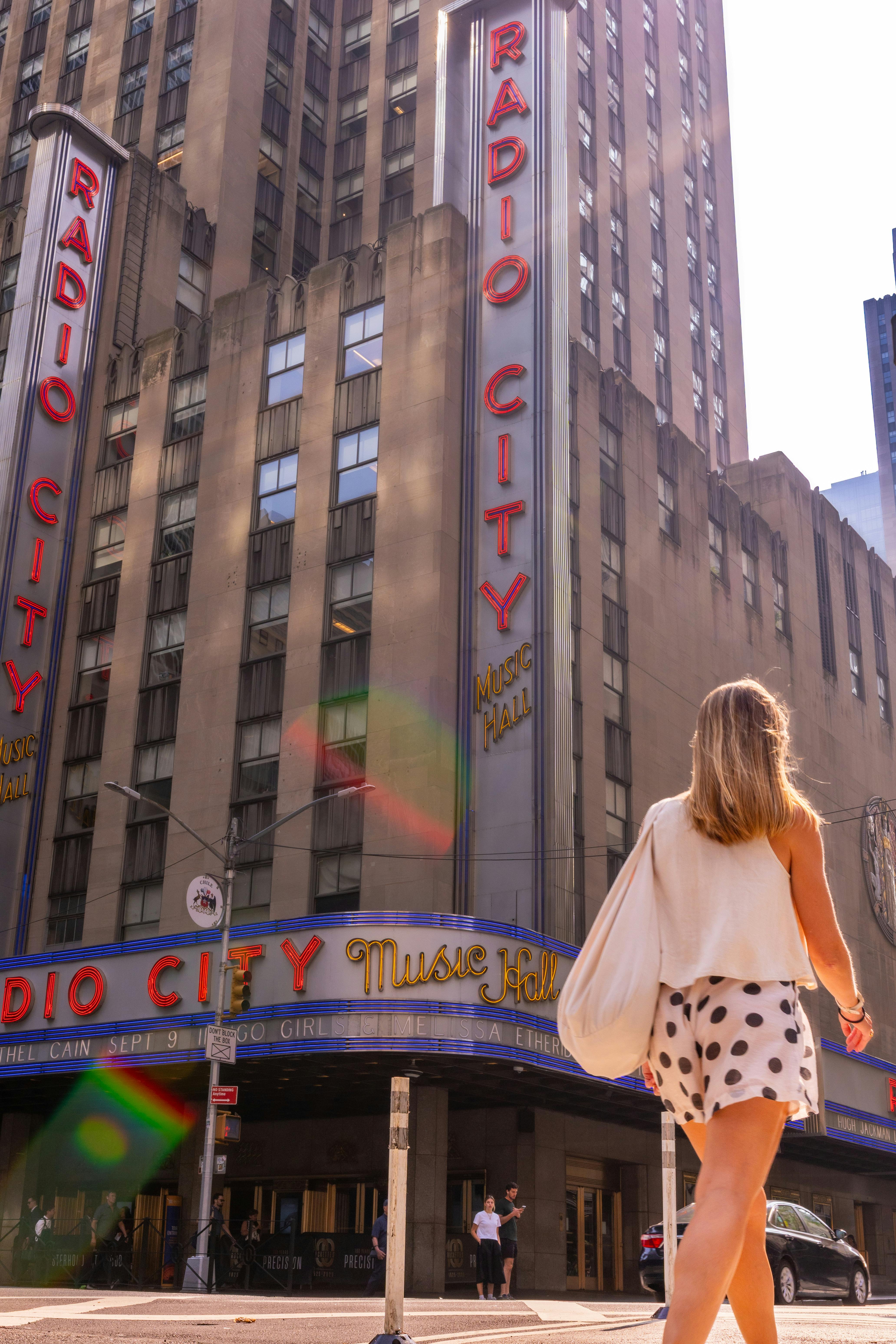 A woman walking near Radio City Music Hall in New York City on a sunny day.