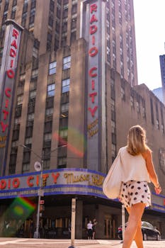 A woman walking near Radio City Music Hall in New York City on a sunny day.