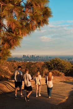 Four people enjoy a hike with a view of the Los Angeles skyline during a sunny day.
