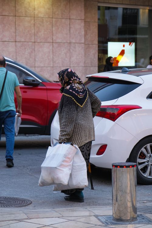Free A woman with shopping bags walks on an urban street near parked cars. Stock Photo