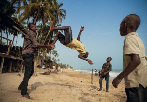 Free Children playing and performing gymnastics on a vibrant beach in Accra, Ghana, under a clear blue sky. Stock Photo