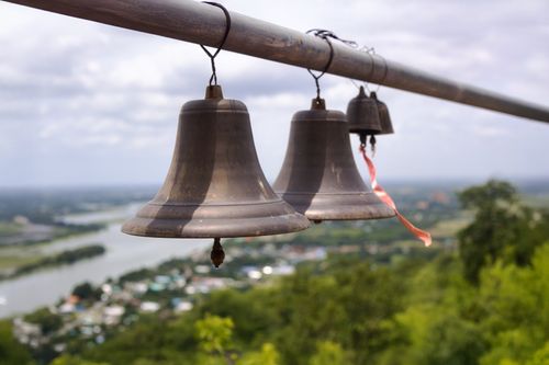 Free Metallic bells suspended outdoors overlooking a river and lush landscape. Stock Photo
