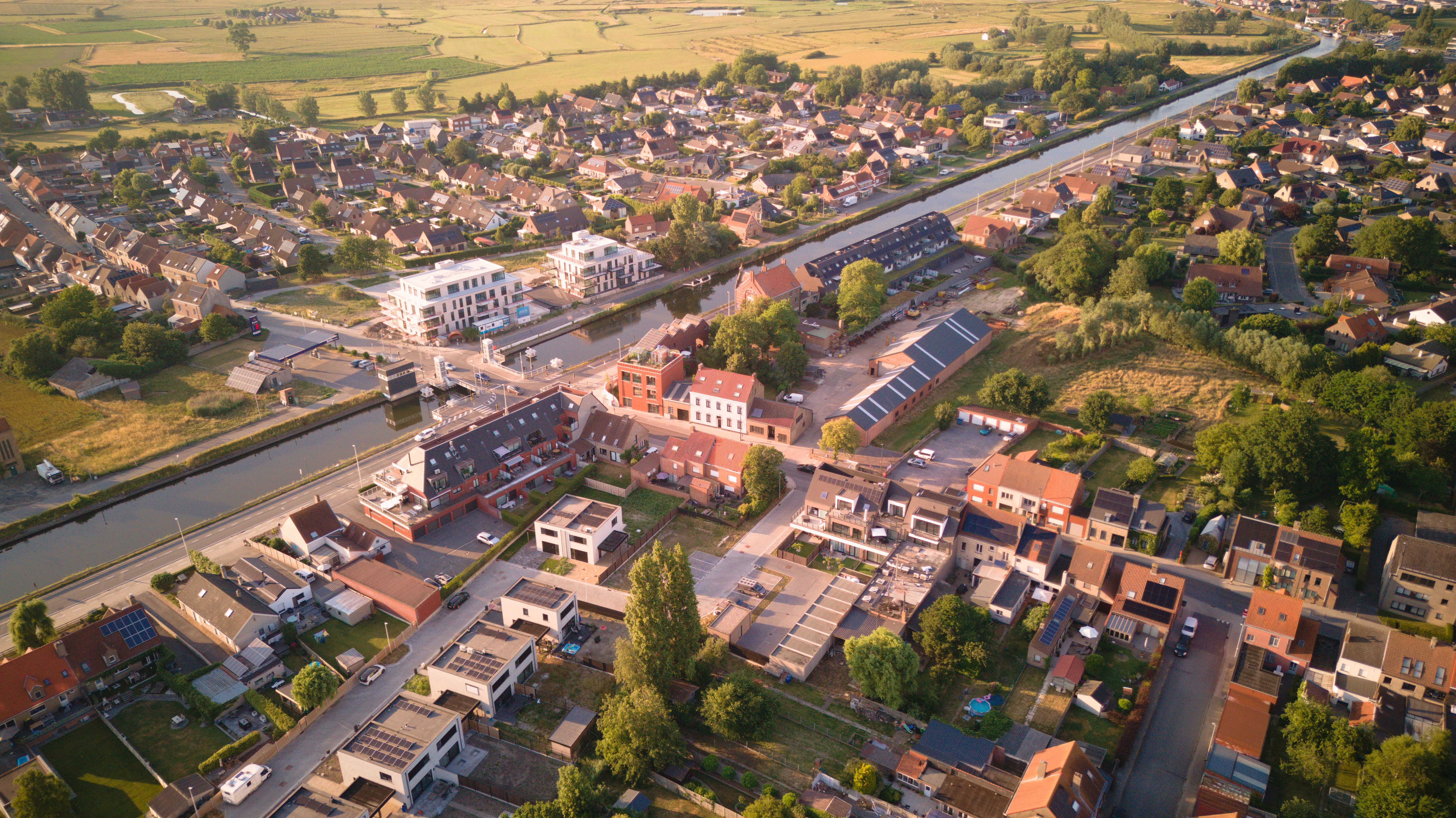 Aerial shot of Oudenburg, Belgium showcasing residential area and canal in summer light.