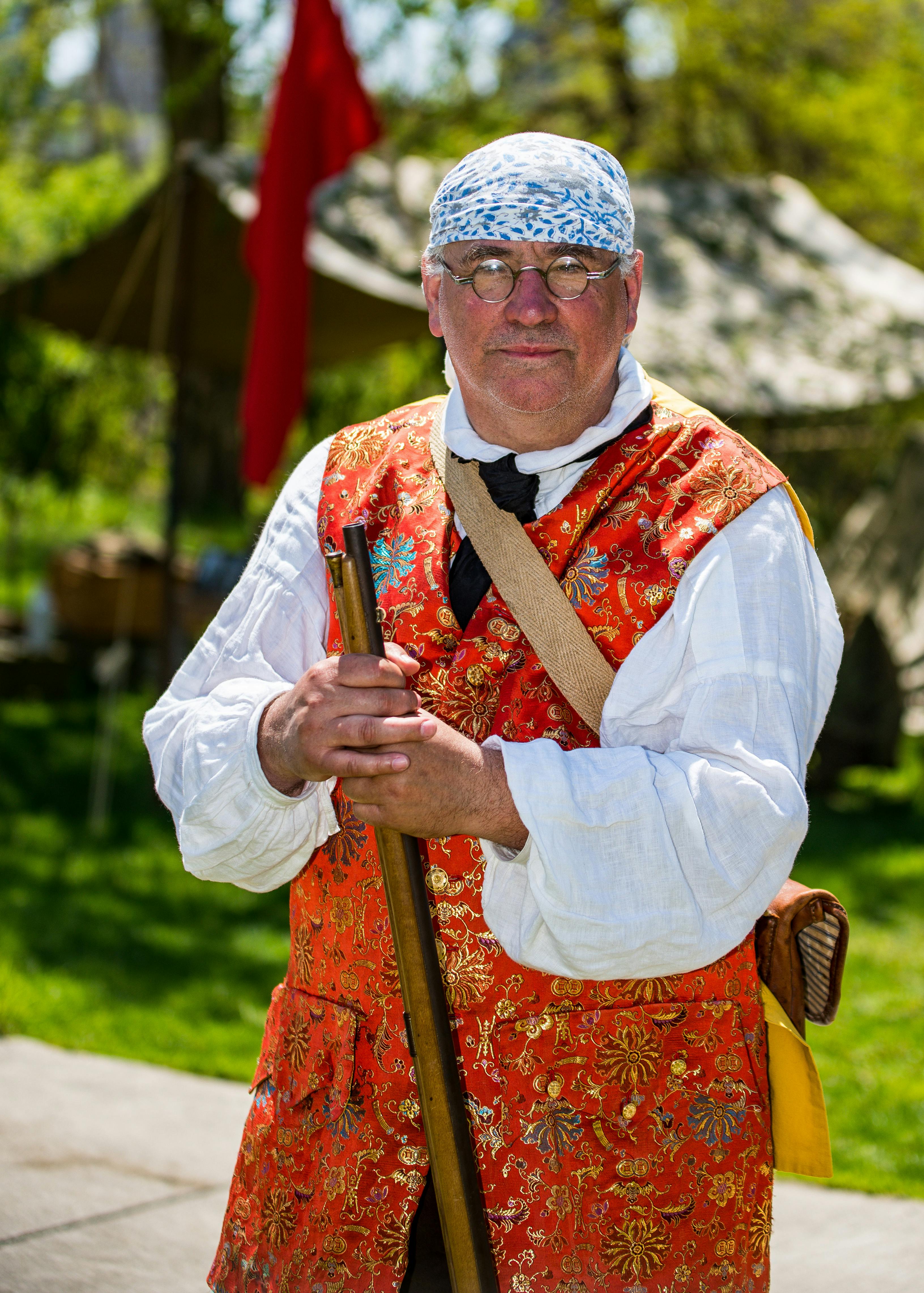 Man dressed in historical attire participates in outdoor reenactment event.