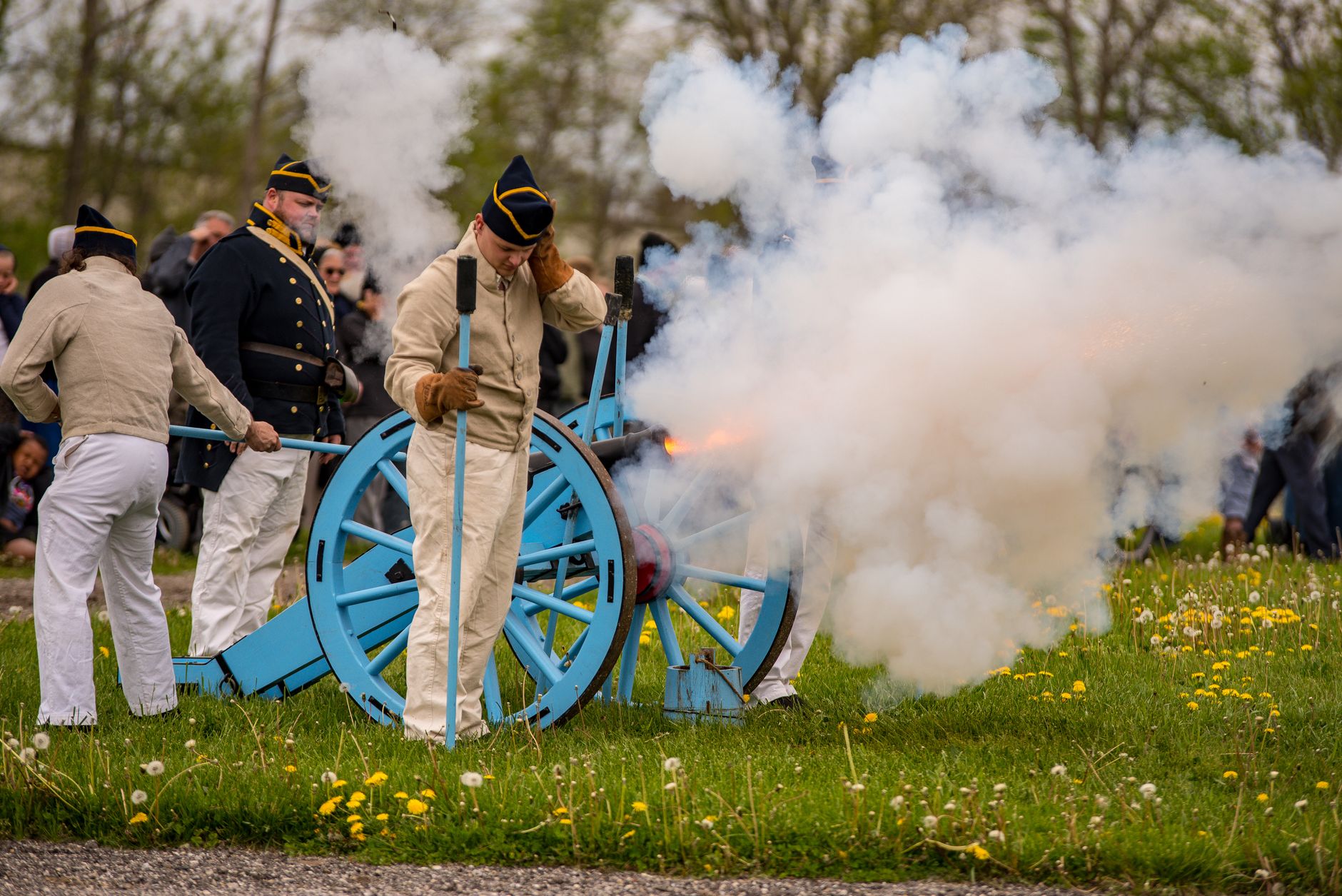 Civil war reenactors fire a cannon, creating a cloud of smoke on a grassy field.