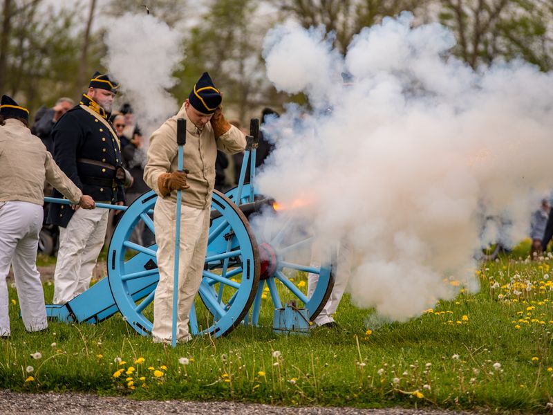 Civil war reenactors fire a cannon, creating a cloud of smoke on a grassy field - battlefields