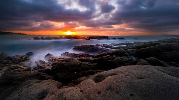 Capture of a stunning sunset over a rocky coastline with vibrant colors and dramatic clouds.