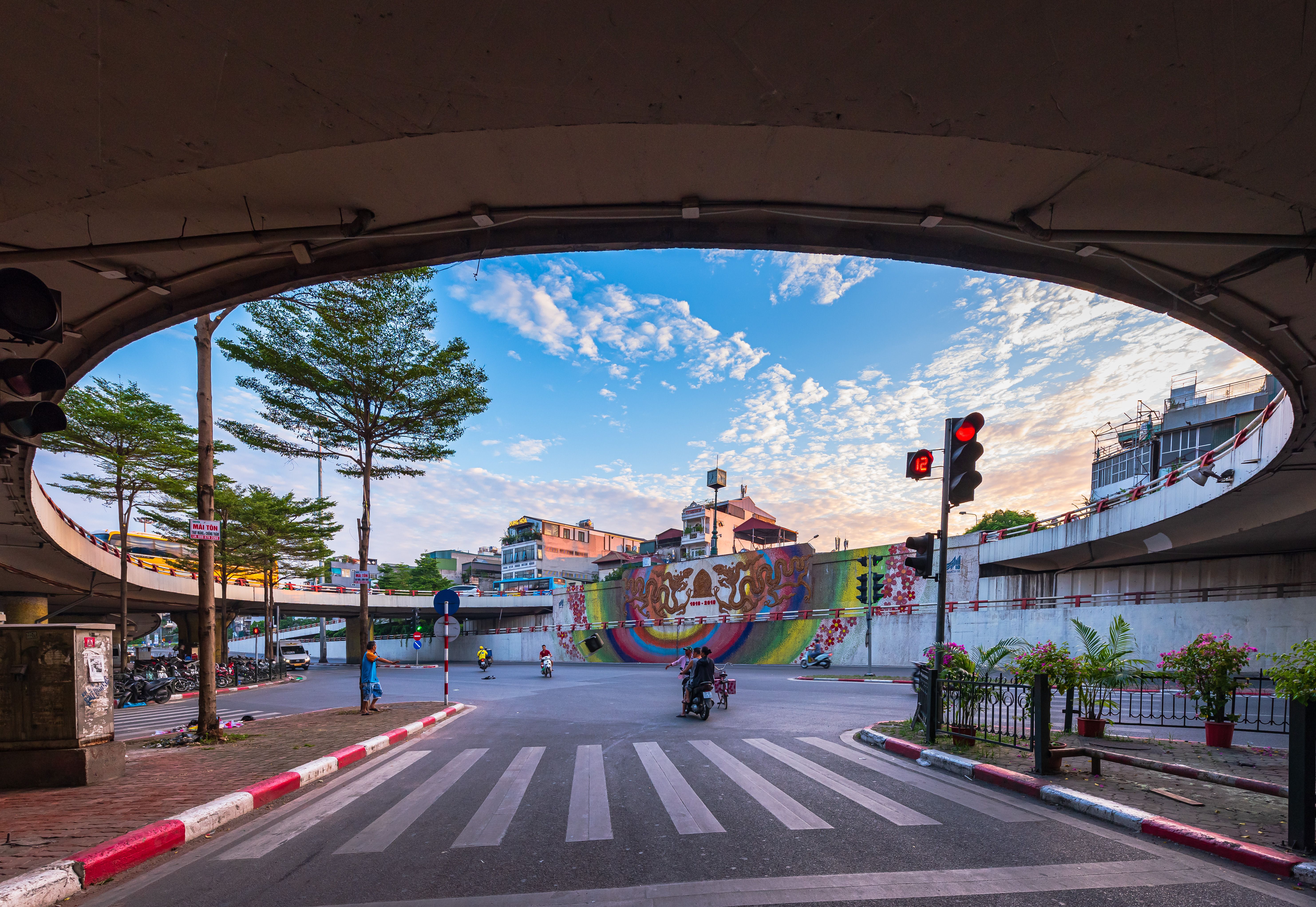 Vibrant city scene under an overpass with colorful mural, traffic lights, and bustling city life.