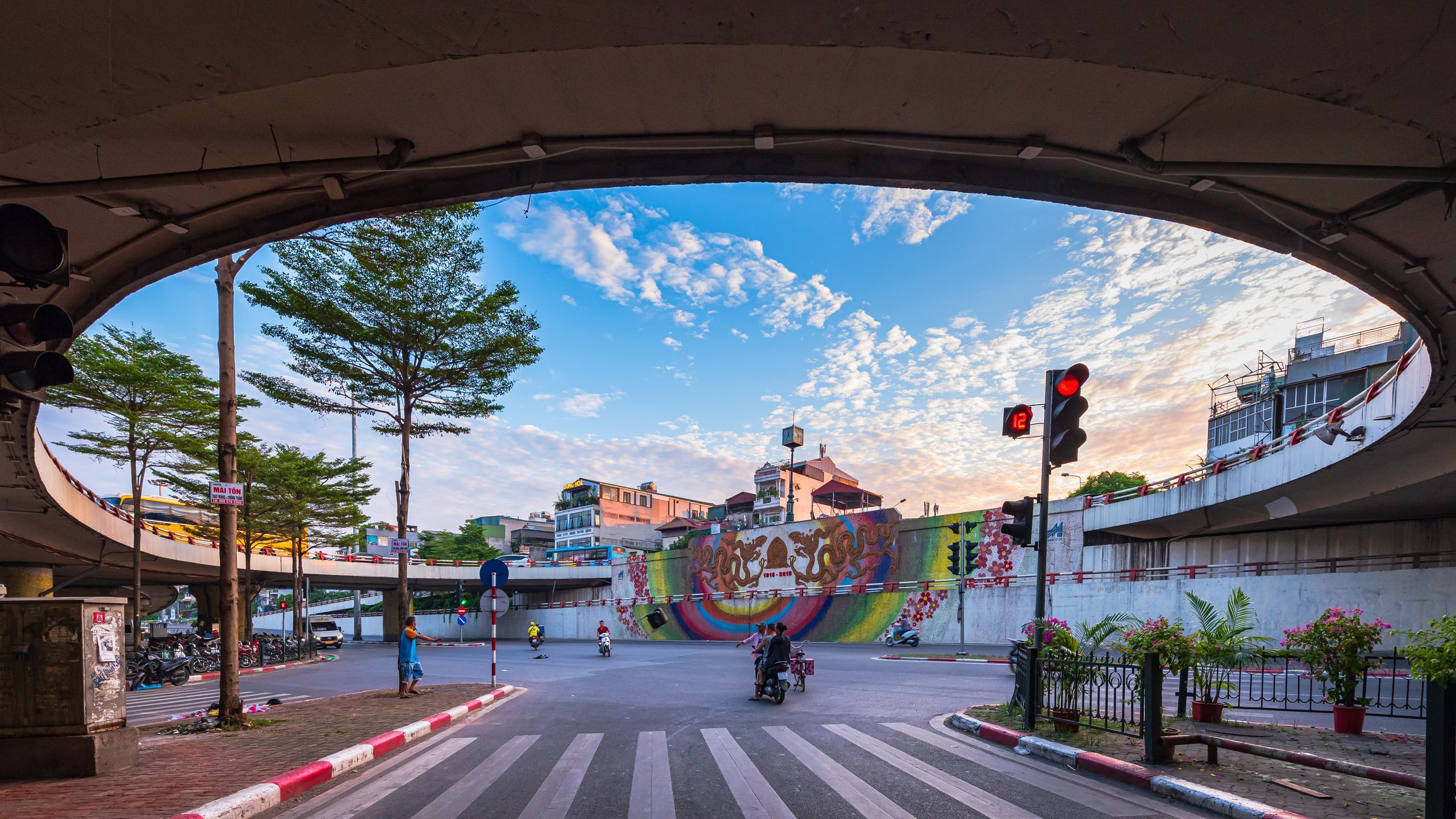 Vibrant city scene under an overpass with colorful mural, traffic lights, and bustling city life.