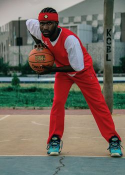 Portrait of a focused male basketball player in sporty attire holding a ball on an outdoor court.