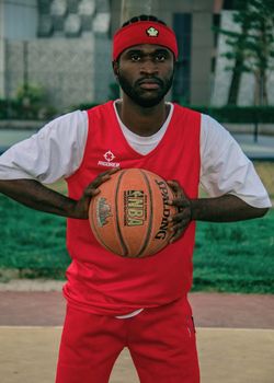 African American male basketball player holding a Spalding ball on an outdoor court.