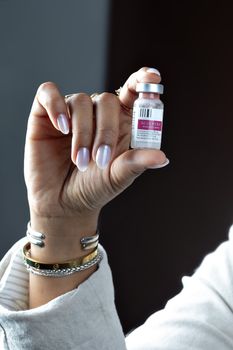 Detail of a person's hand holding a Sculptra cosmetic vial against a dark background.