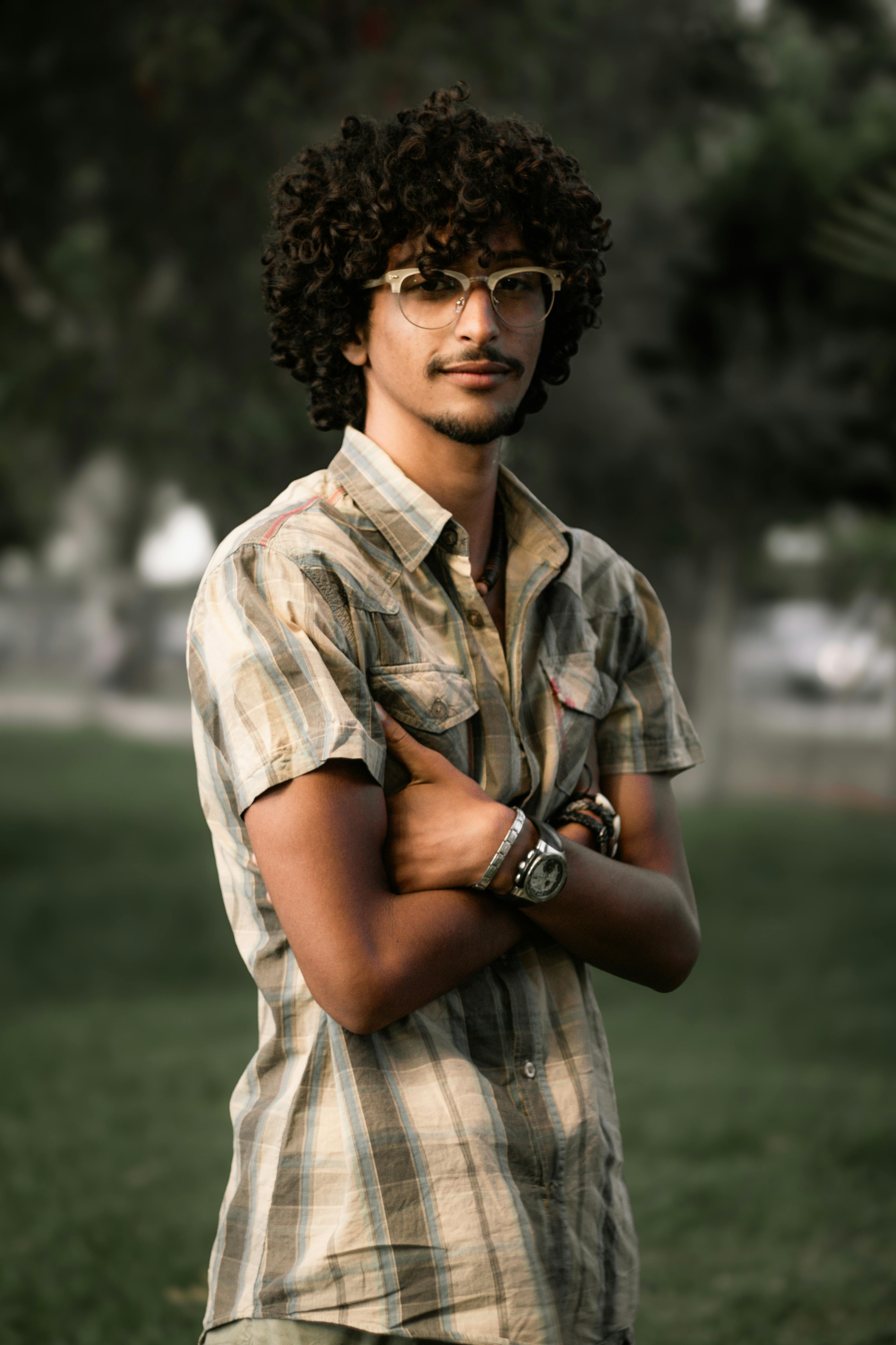 Miễn phí Người đàn ông tóc xoăn mặc trang phục thường ngày, đeo kính, tự tin tạo dáng ngoài trời vào mùa hè. Ảnh lưu trữ