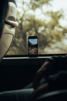 Smartphone placed on bus window sill recording scenic outdoors, blurred background.