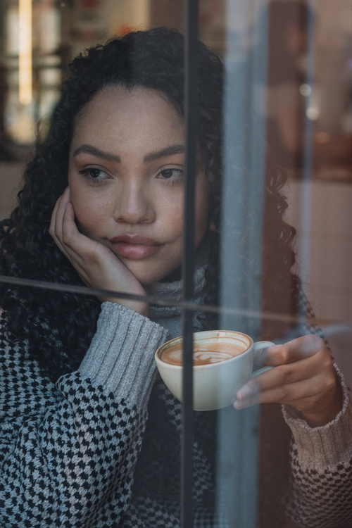 Free Pensive woman holding coffee cup, gazing outside through a window. Stock Photo
