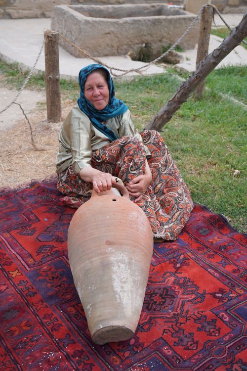 Free Woman sitting on a vibrant rug outdoors with a large clay vessel, showcasing cultural heritage. Stock Photo