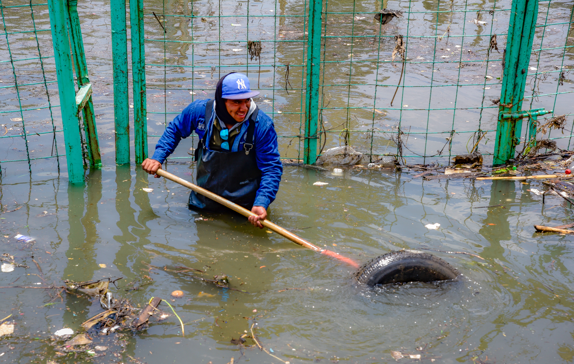 Man removing debris from flooded polluted water with a stick, highlighting urban pollution.