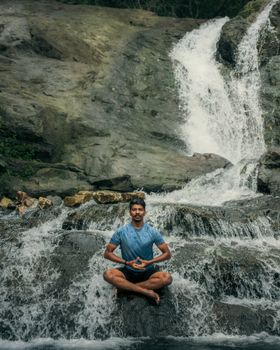 A serene scene of a man meditating in lotus position by a waterfall, promoting mindfulness and tranquility.