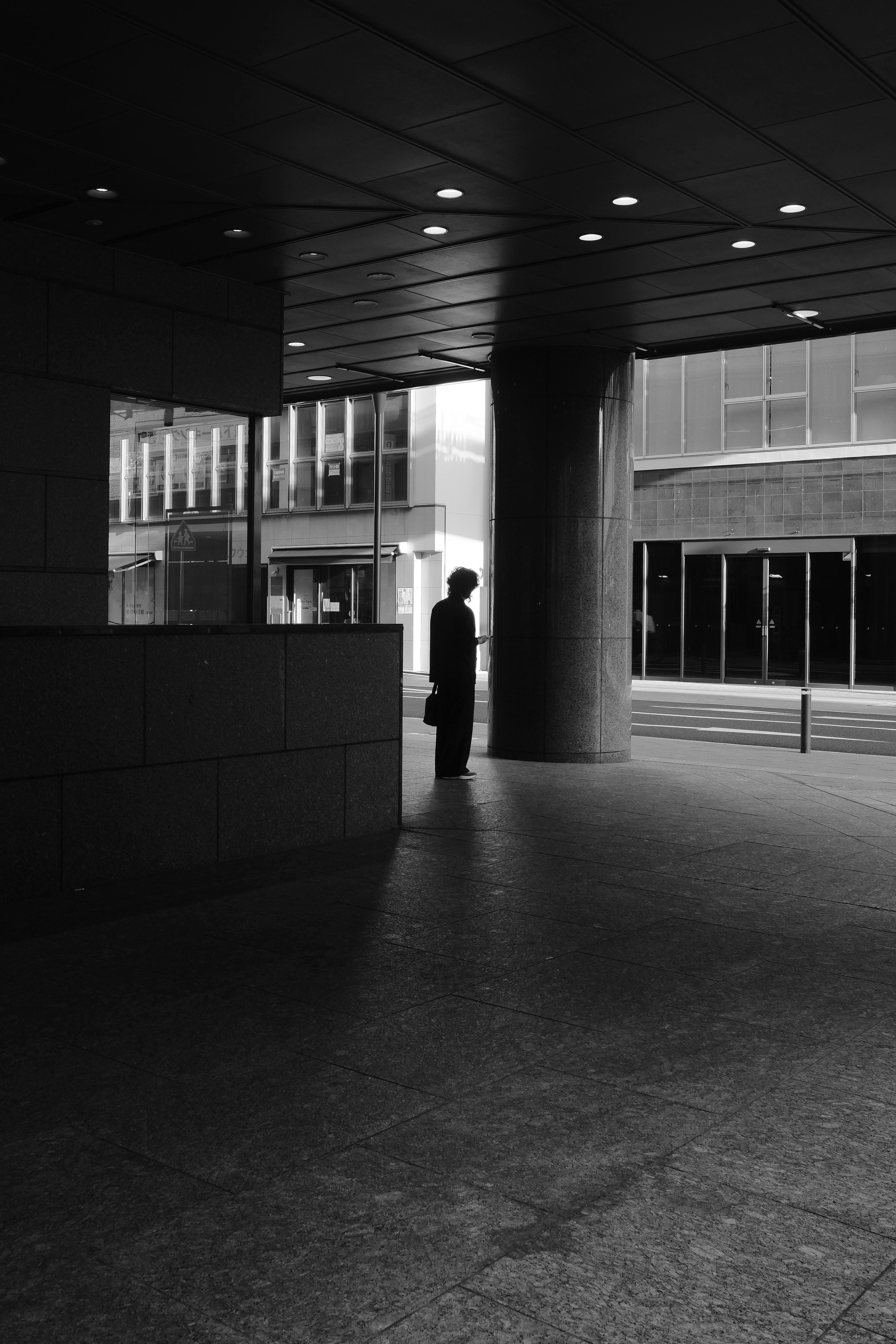 A black and white photo of a solitary silhouette in a modern urban setting, exuding a moody atmosphere.
