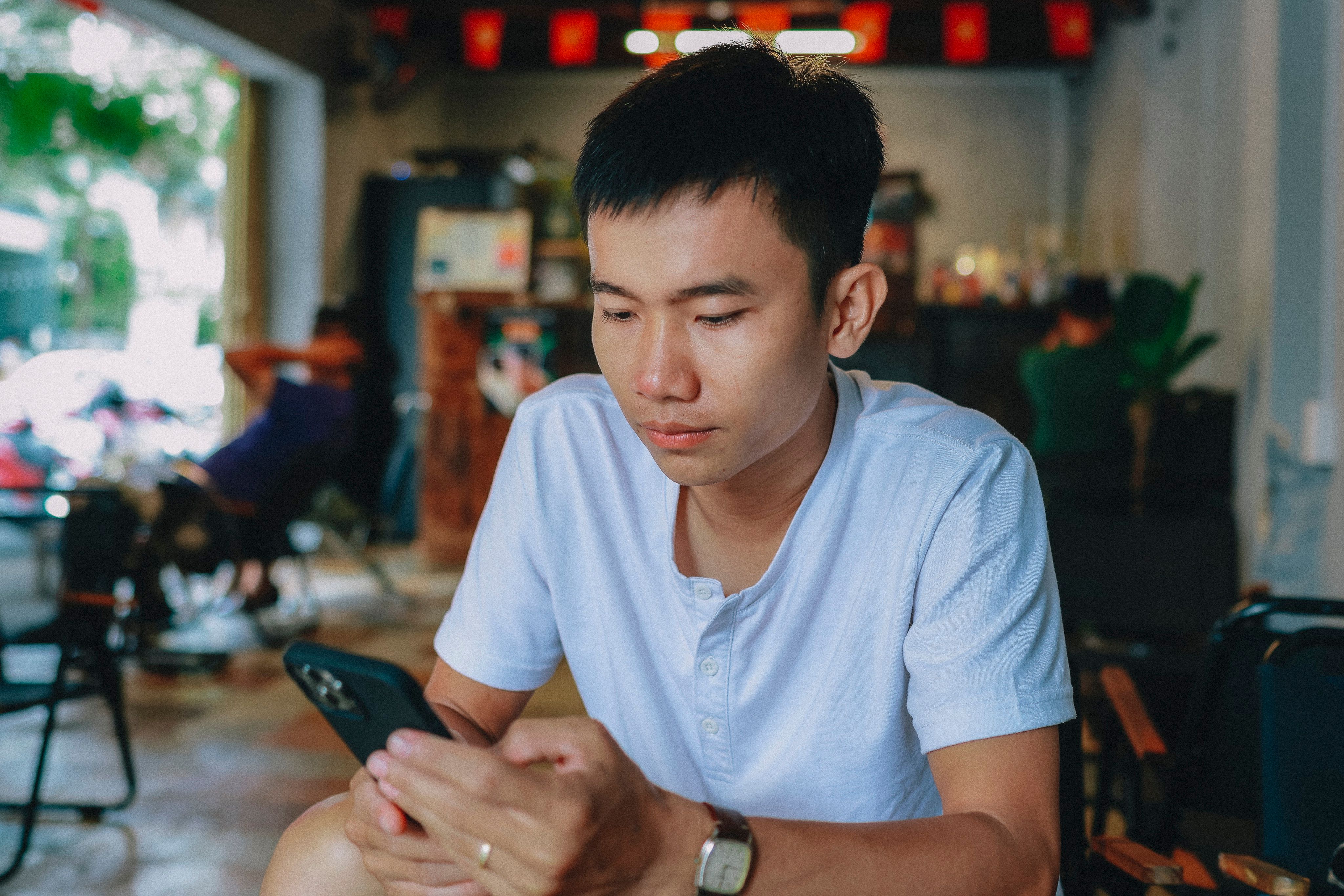 Young Man Engaging with Smartphone in Cozy Cafe