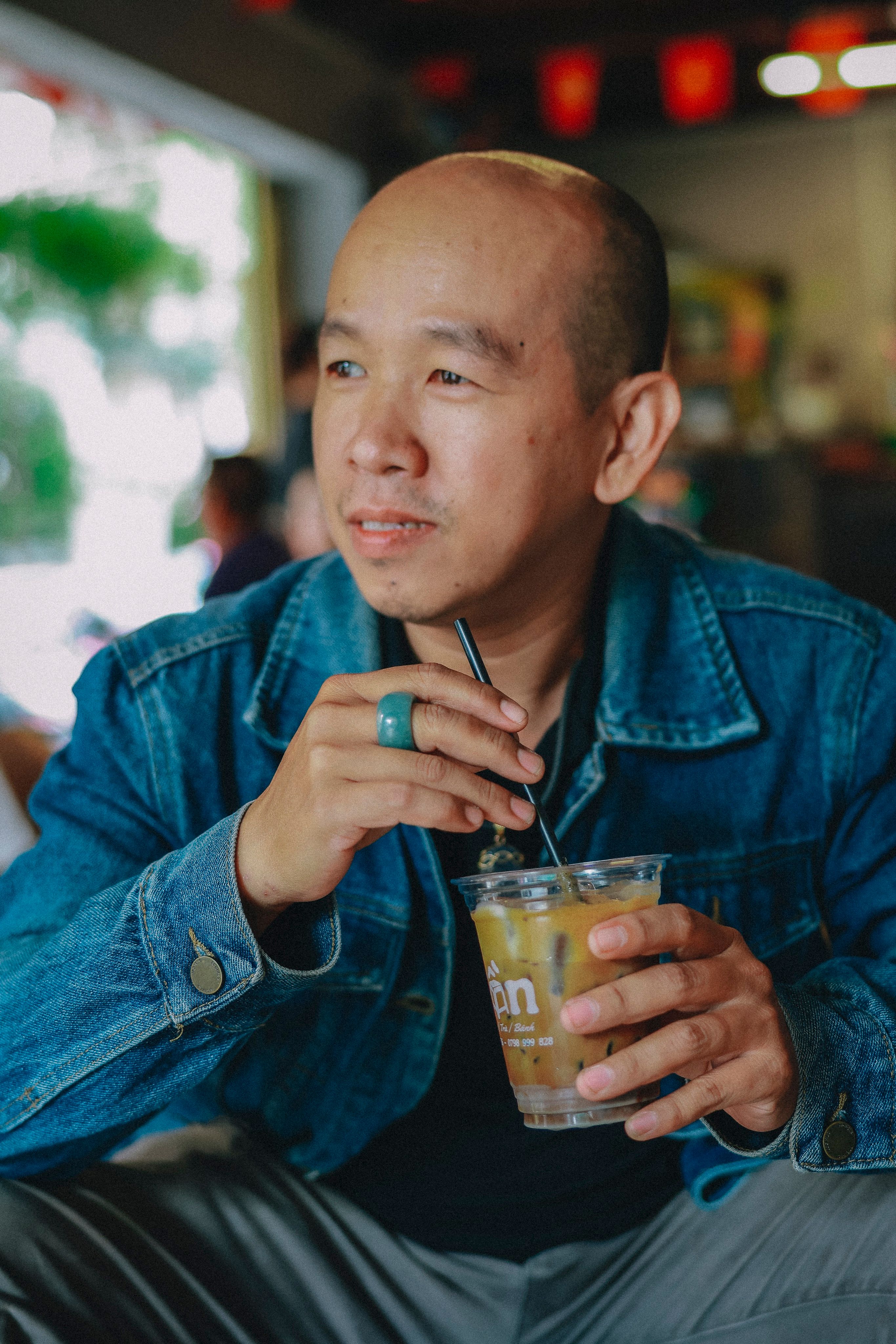 Relaxed man in denim jacket sipping a cold beverage in a cozy café setting.
