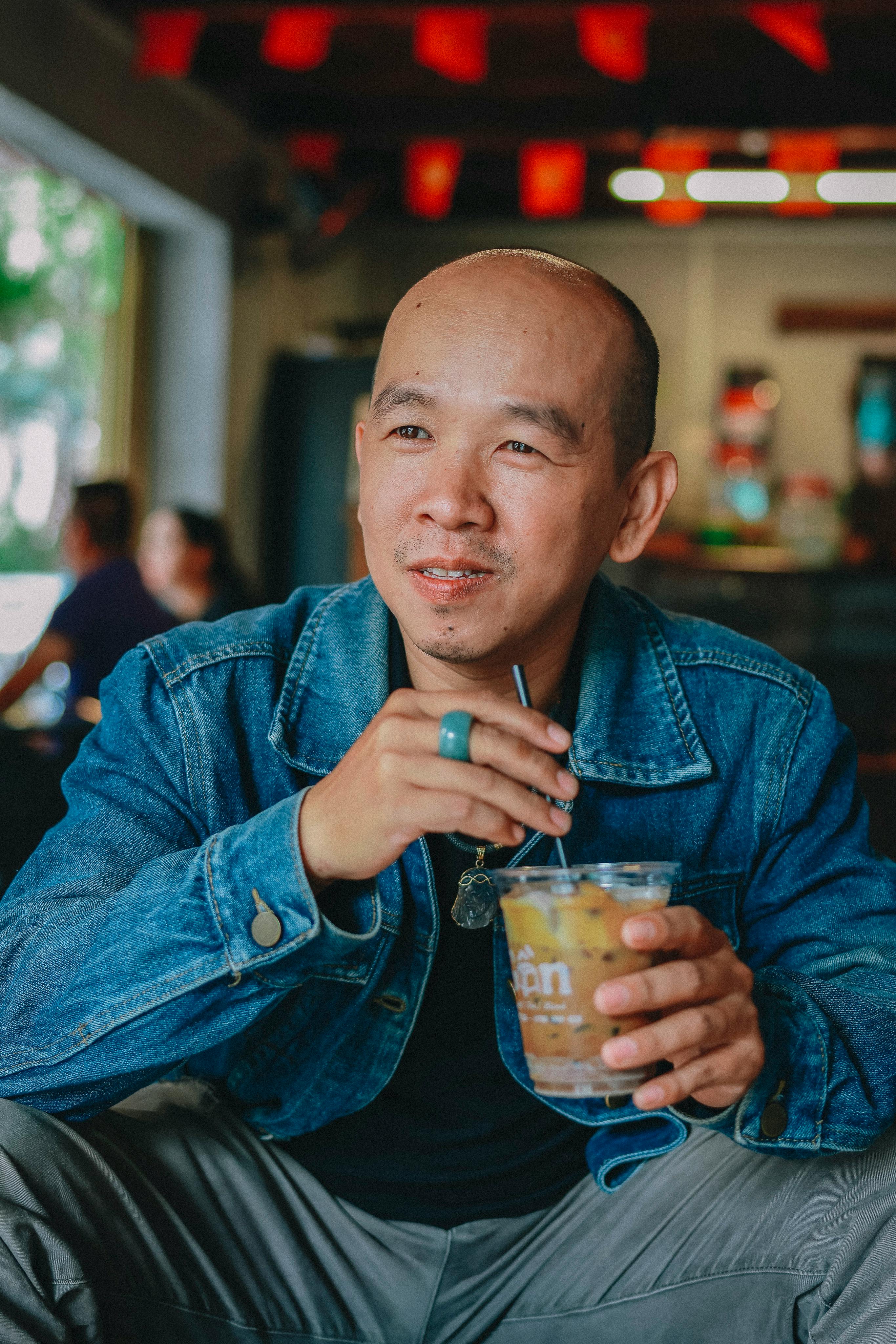 Free Smiling man in denim jacket enjoying a drink inside a cozy cafe. Stock Photo