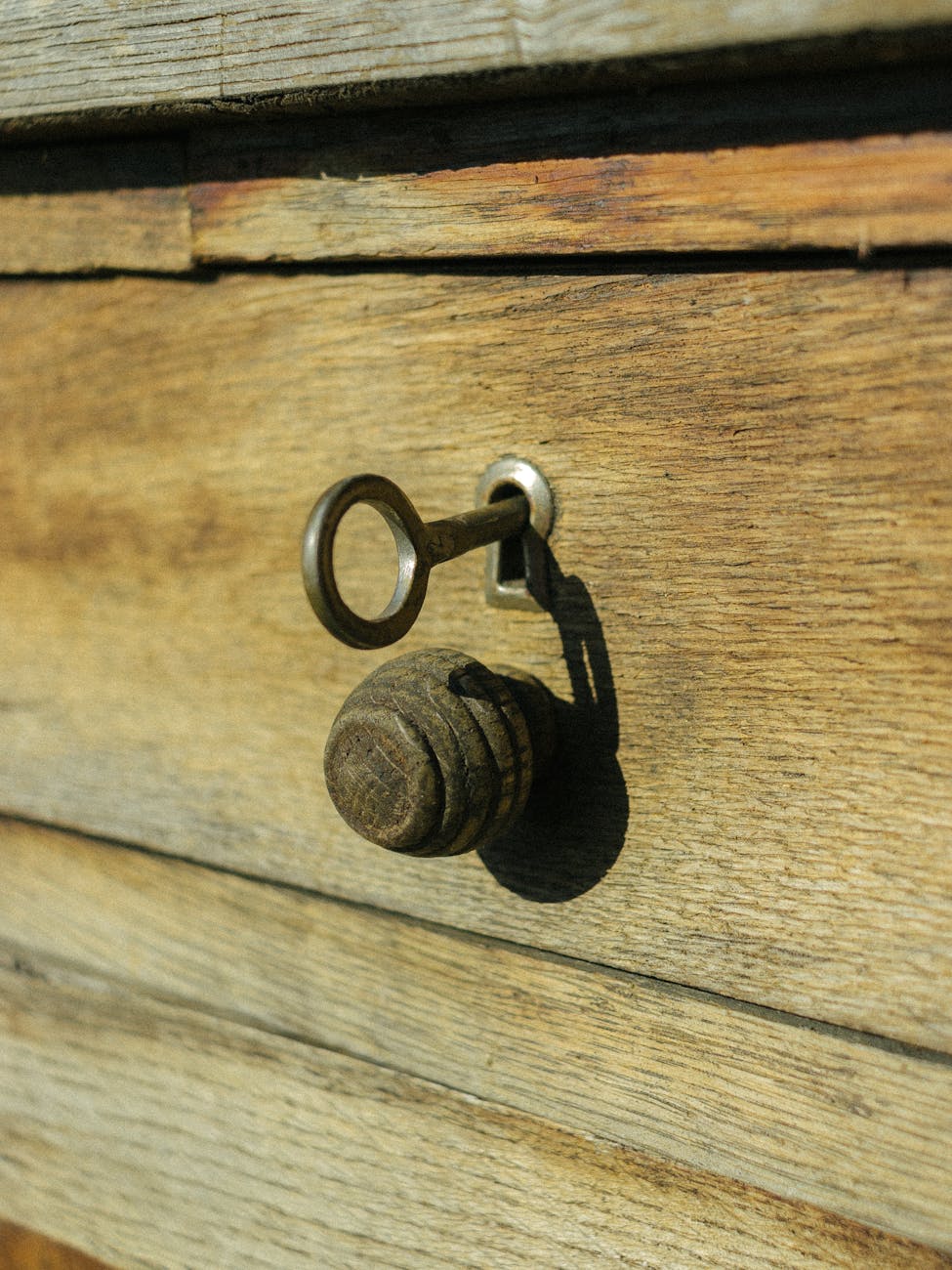 Close-up of an antique key inserted into a rustic wooden surface under bright daylight.