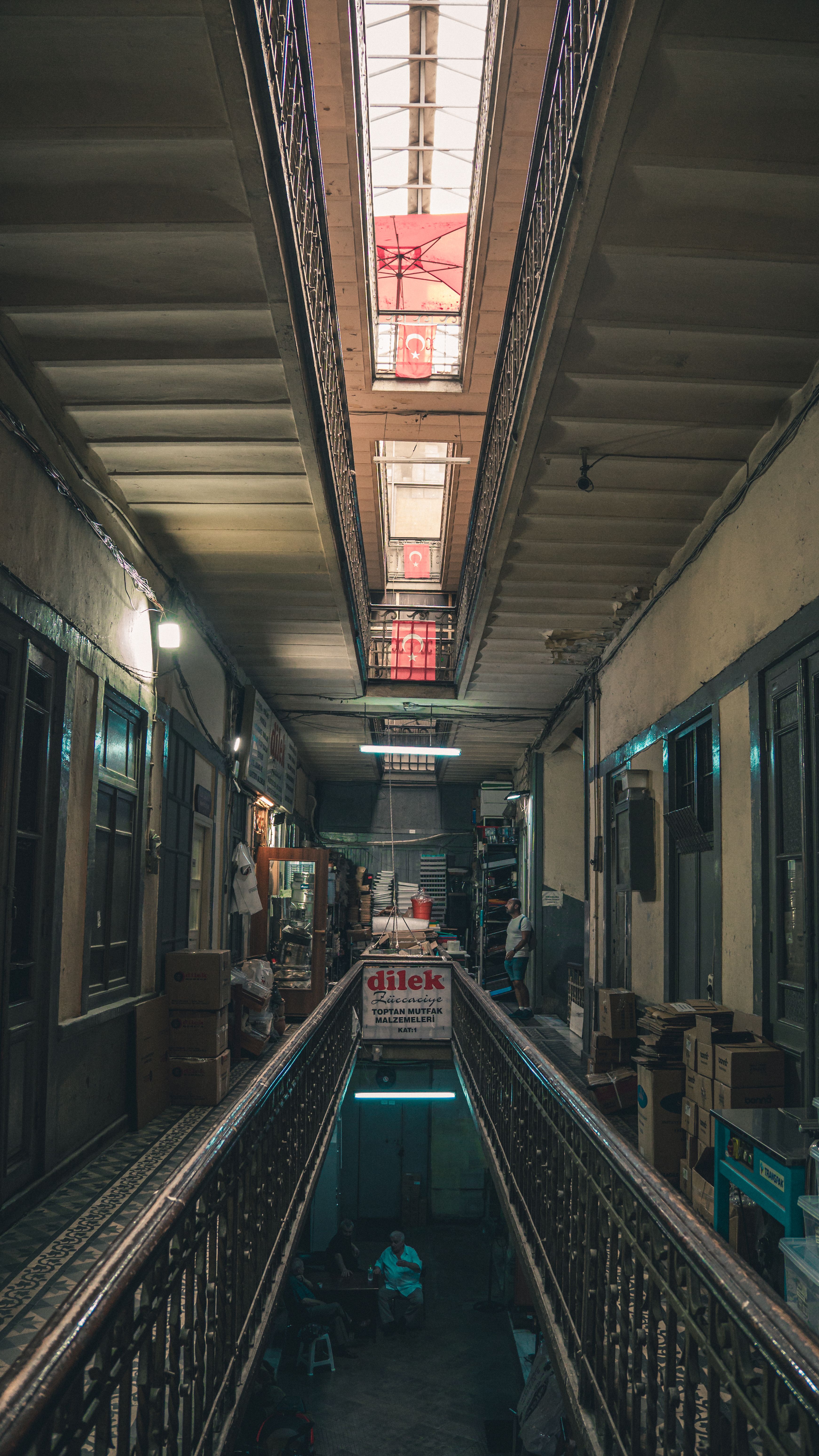 A narrow indoor hallway of a historic market with a skylight illuminating stacked boxes and shops.