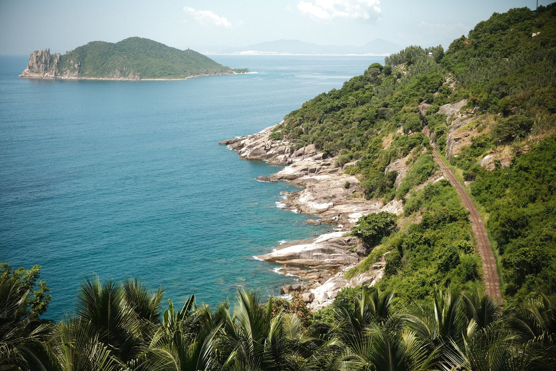 A breathtaking view of a coastal path with lush greenery and a distant island in bright daylight.