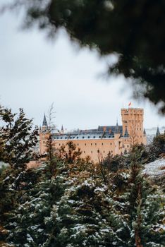 A picturesque winter view of the Alcázar of Segovia, surrounded by snow-covered trees.