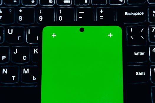 A close-up of a smartphone with a green screen placed on a laptop keyboard.
