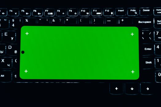 A smartphone with a green screen sits on a lit keyboard, ideal for chroma key editing.