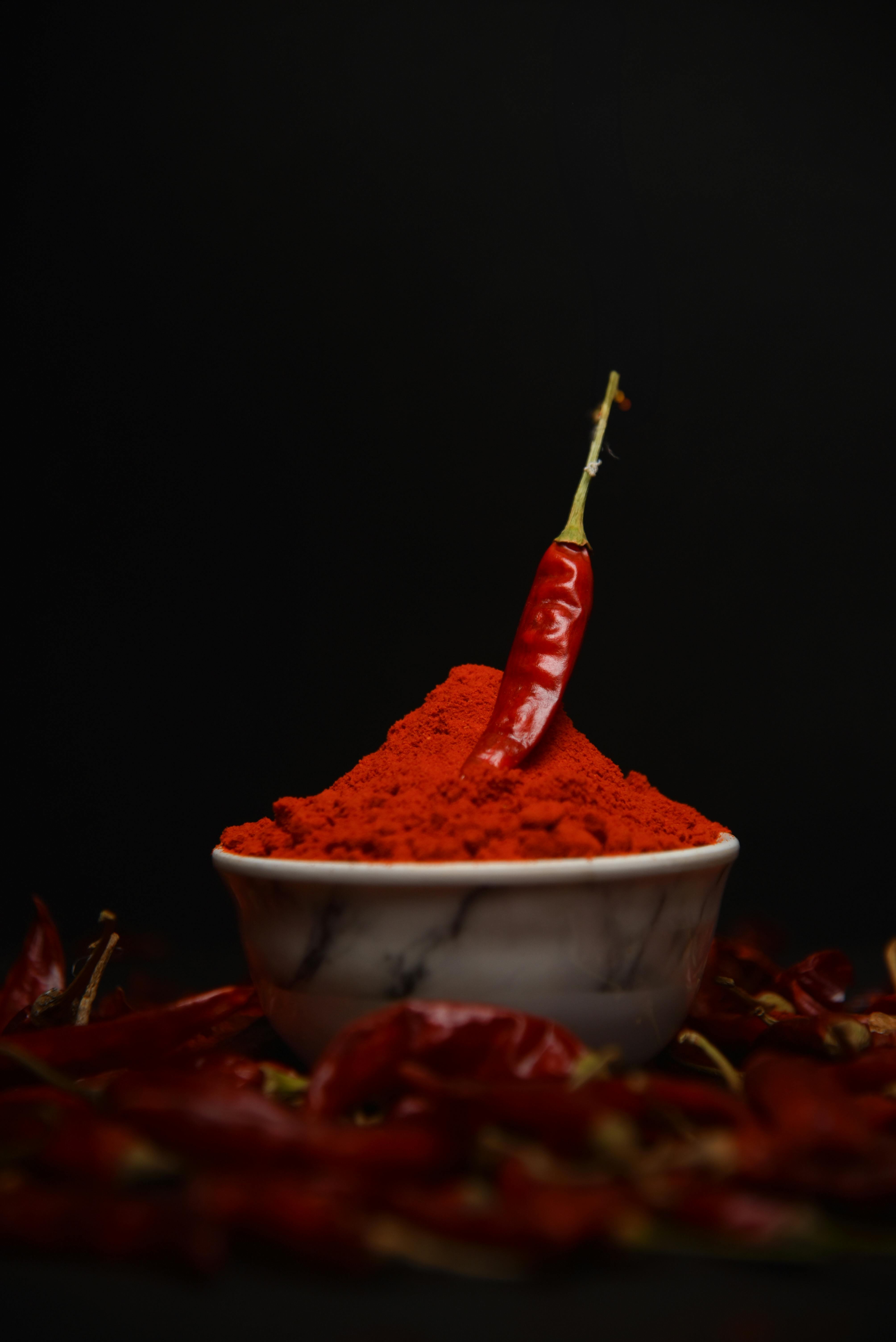 A single chili pepper sits atop a bowl of vibrant red chili powder, surrounded by dried chilies.