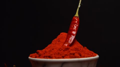 A single chili pepper sits atop a bowl of vibrant red chili powder, surrounded by dried chilies.