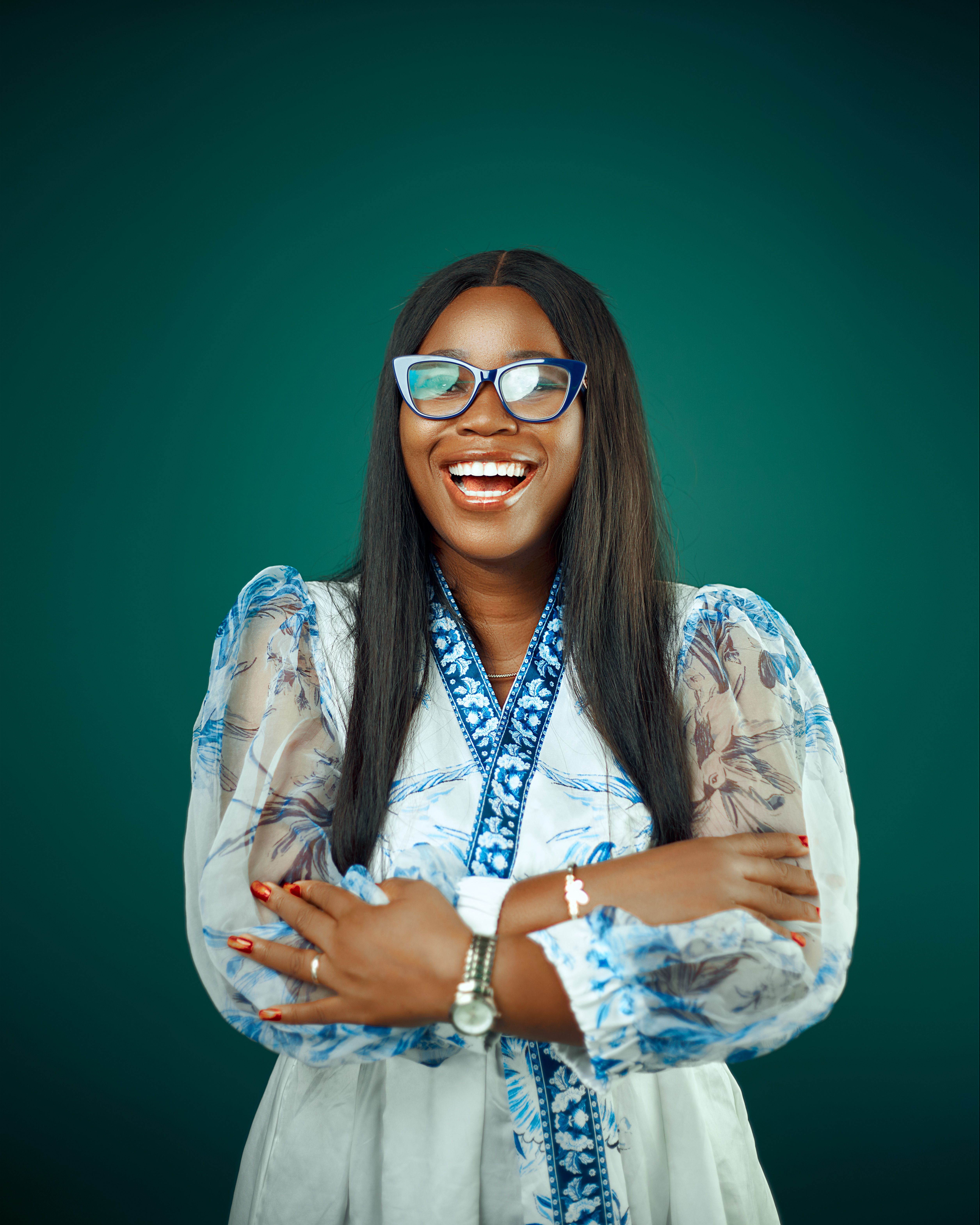 A cheerful woman in glasses and a blue floral dress against a deep green background.