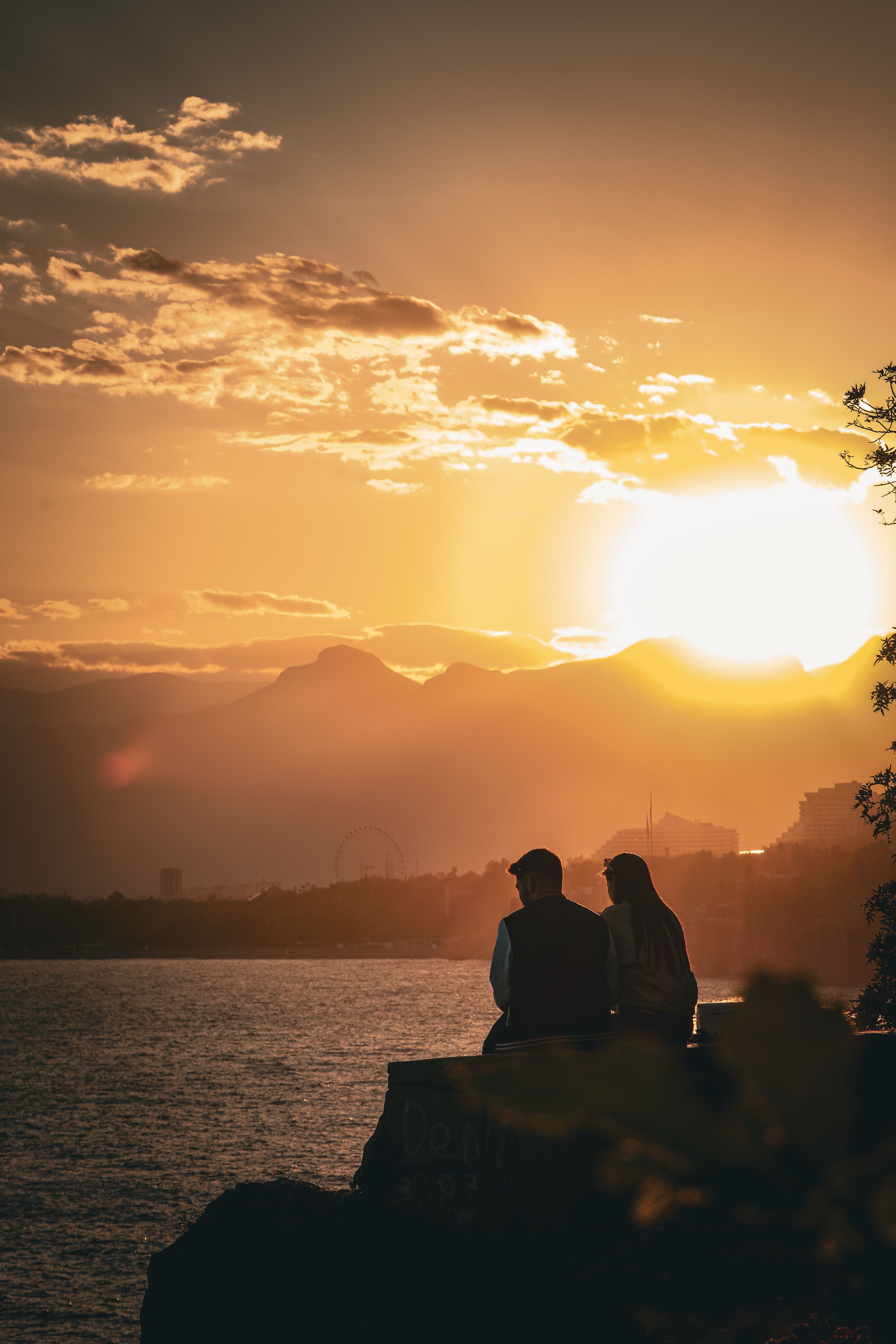 A couple enjoys a breathtaking sunset over Antalya's coastline, with stunning mountain views and serene waters.