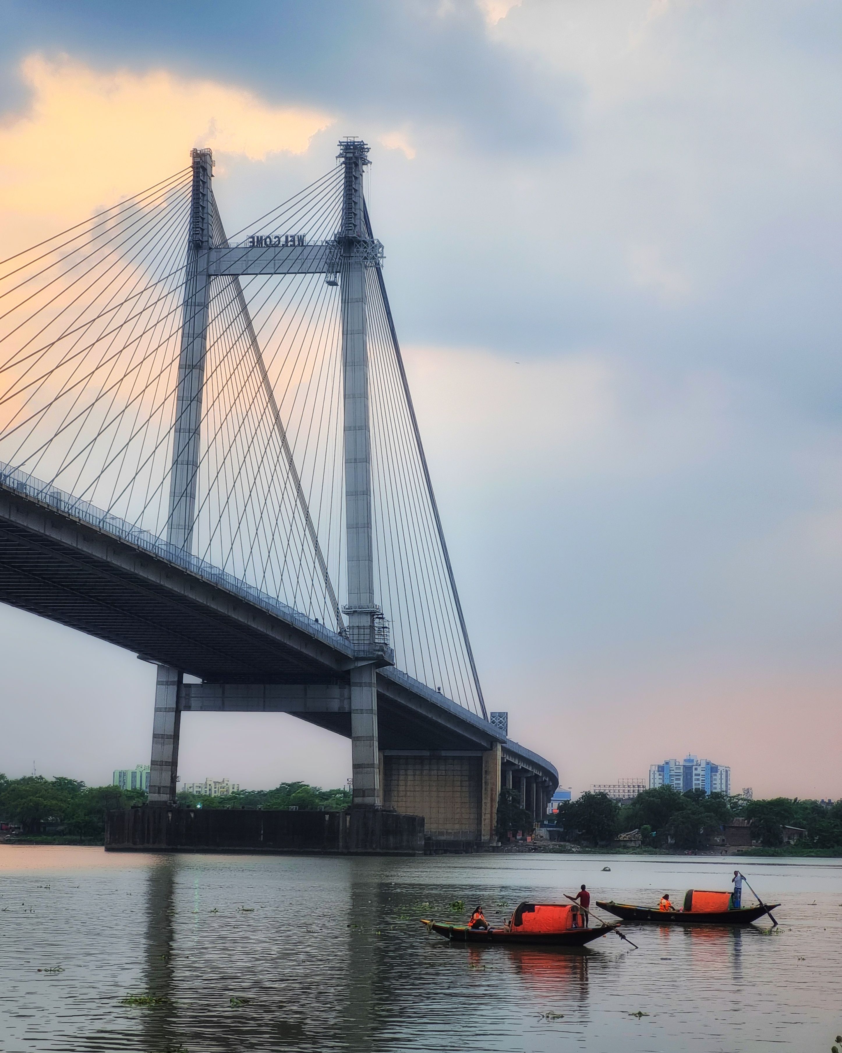 Small boats beneath a suspension bridge at sunset, capturing serene water scenes near an urban landmark.