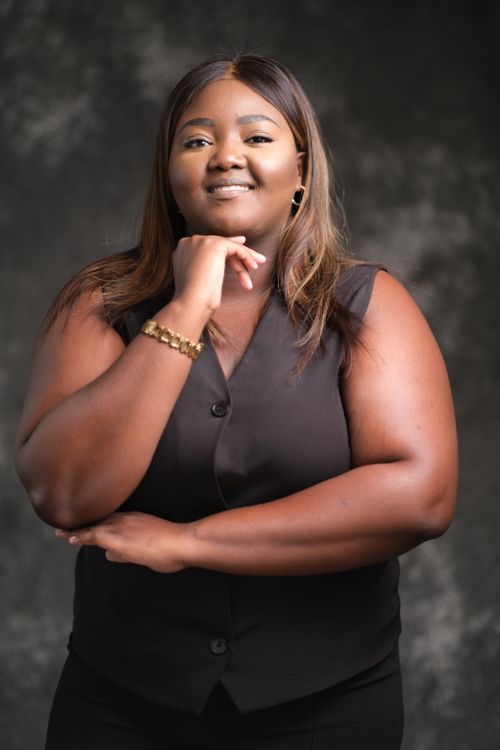 Free Portrait of a confident woman posing with a thoughtful expression, wearing a black vest against a dark background. Stock Photo