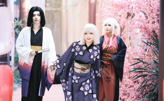 A group of cosplayers in traditional attire pose among cherry blossoms, embodying anime characters.
