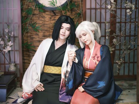 A couple in traditional Japanese cosplay holding hands in a serene indoor setting.